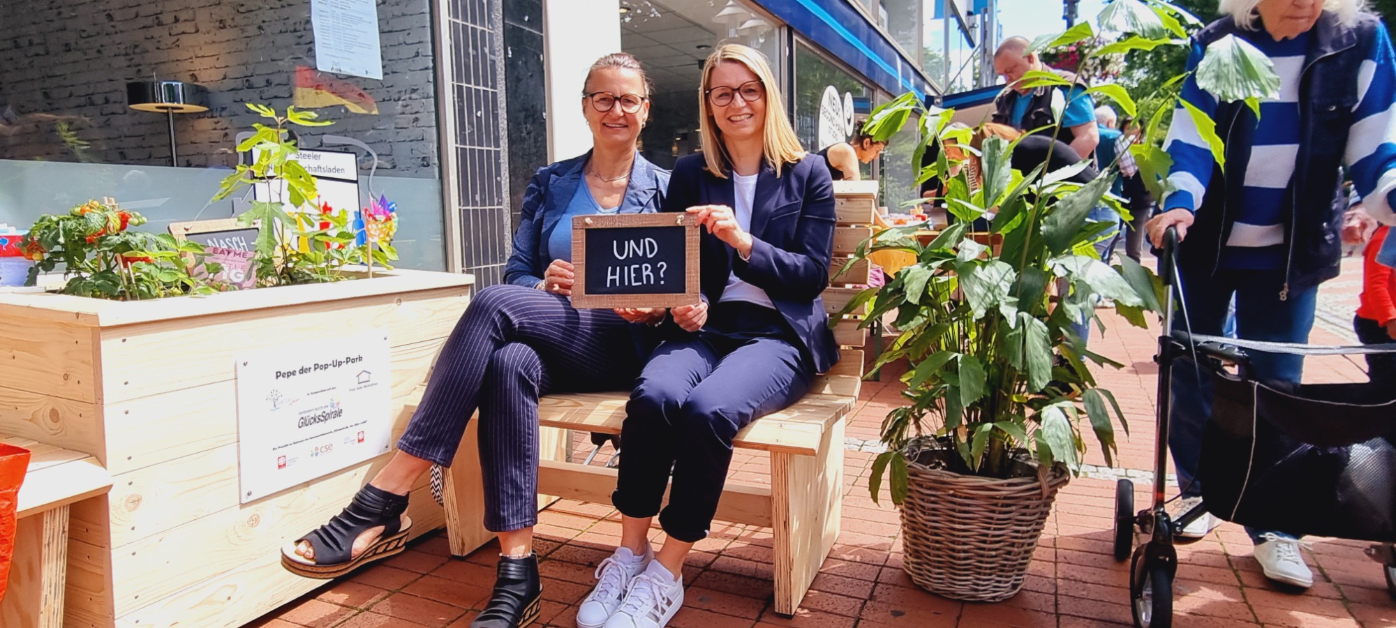 Hochbeet, daneben Holzbank mit zwei Personen